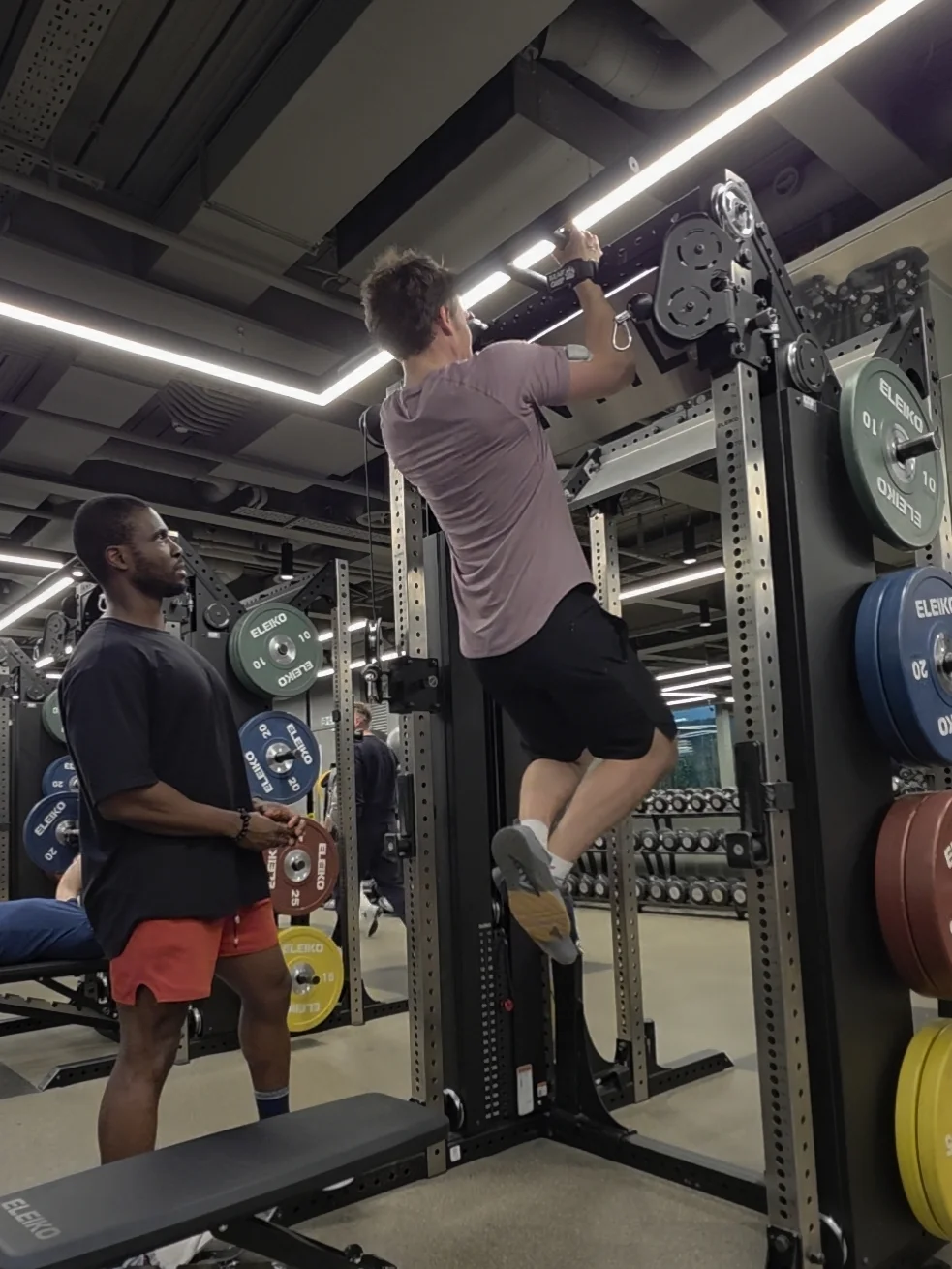 Femi coaching a client through a pull-up exercise in the gym